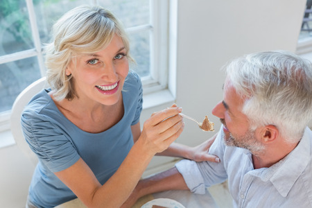 High angle view of a smiling woman feeding mature man pastry at homeの写真素材