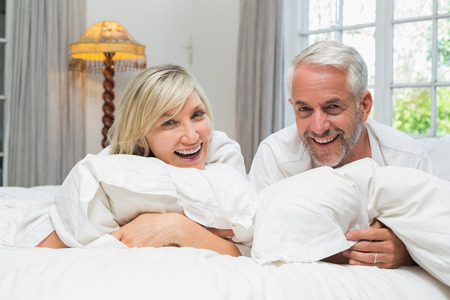 Portrait of a happy mature couple lying in bed at homeの写真素材