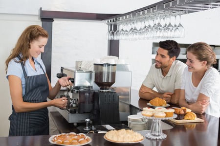 Side view of a smiling couple looking at waitress prepare coffee at the coffee shopの写真素材