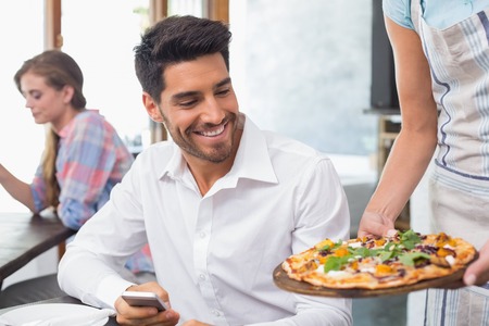 Waitress giving pizza to a smiling young man at the coffee shopの写真素材