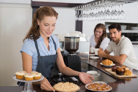 Female cafe owner holding sweet snacks with couple at counter in the coffee shopの写真素材