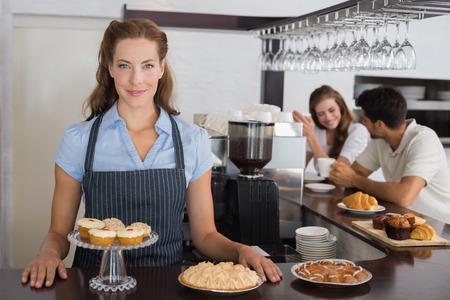 Portrait of a smiling female cafe owner with sweet snacks and couple at counter in the coffee shopの写真素材