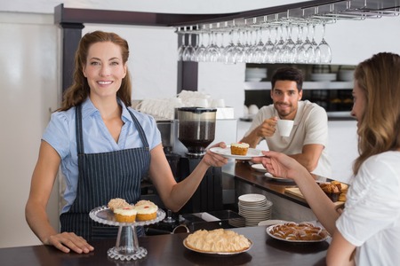 Portrait of a smiling female cafe owner with sweet snacks and couple at counter in the coffee shopの写真素材