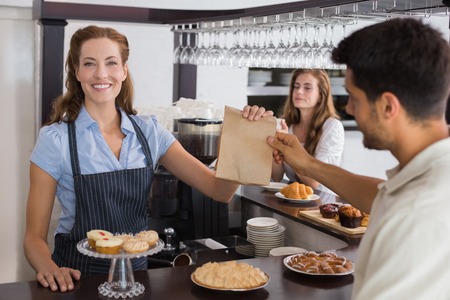 Friendly female cafe owner giving packed food to a couple at the coffee shopの写真素材