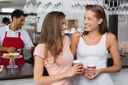 Cheerful female friends with male barista at counter in the coffee shopの写真素材