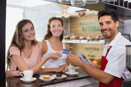 Smiling young friends with woman holding out credit card at the coffee shopの写真素材