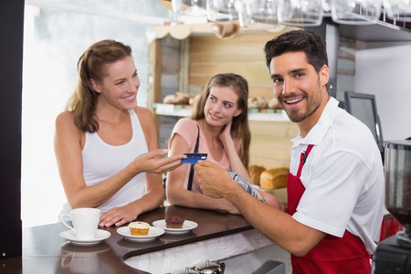 Smiling young female friends paying bill at coffee shop using card billの写真素材