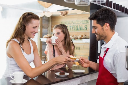 Side view of a male barista giving pastry to woman at counter in the coffee shopの写真素材