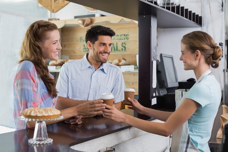 Side view of a smiling waitress giving coffee to a couple at the coffee shopの写真素材