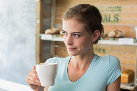 Thoughtful young woman drinking coffee in the coffee shopの写真素材