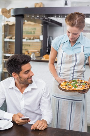 Waitress giving pizza to a smiling young man at the coffee shopの写真素材