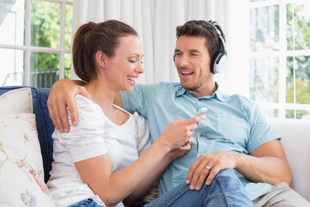 Relaxed young couple listening music with mobile phone on couch at homeの写真素材