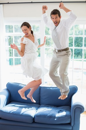 Side view of a cheerful young couple jumping on couch at homeの写真素材