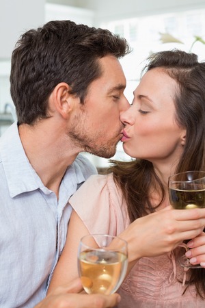Close-up of a loving young couple with wine glasses kissing at homeの写真素材