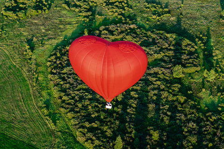 Red balloon in the form of heart over green fields and forestsの写真素材