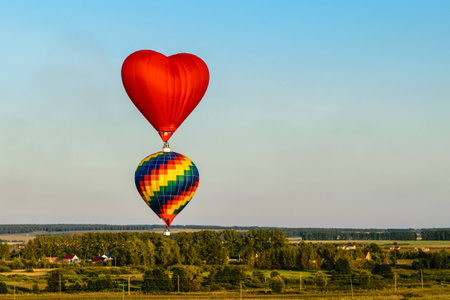 Colorful hot air balloons flying over the village, forest and fieldsの写真素材
