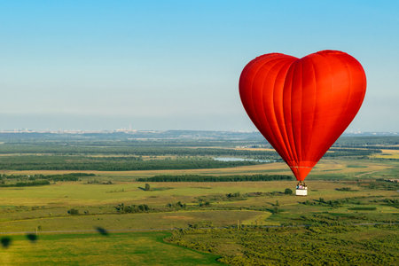 Red balloon in the form of heart over green fields and forestsの写真素材