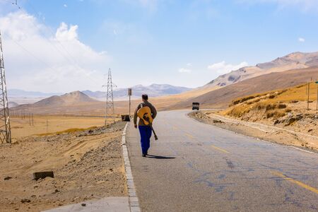 A man with a guitar walks along the road on the Tibetan plateau