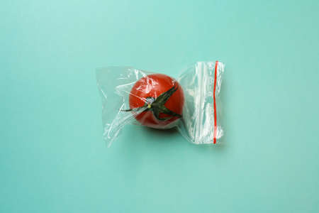 Red tomato in a zip bag on a green background, the concept of excess food packagingの写真素材