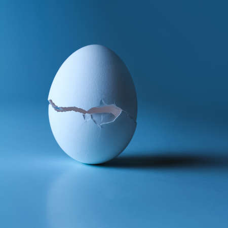 Egg with a crack in the center on a blue backgroundの写真素材