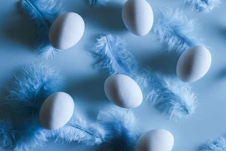 Eggs and feathers in a chaotic pattern on a blue background, top view, minimalism, easter flat layの写真素材