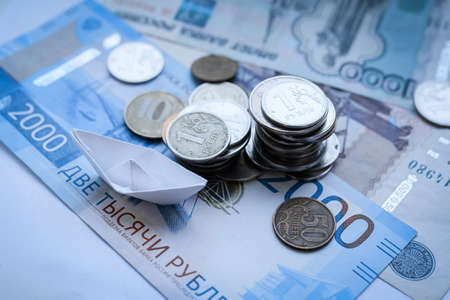 Background from paper and metal coins and a paper boat, rubles background, money for a sea voyage