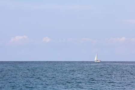 Minimalistic seascape with a strip of sea, sky and a lonely sailboatの写真素材