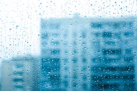 Window covered with water drops with houses in the background, rain in the cityの写真素材