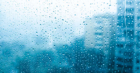 Window covered with water drops with houses in the background, rain in the city