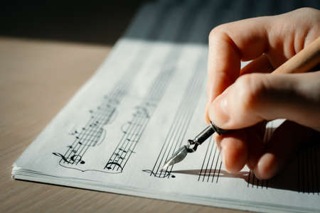 Handwritten notes and female hand holding a pen and writing notes, composing music, selective focusの写真素材