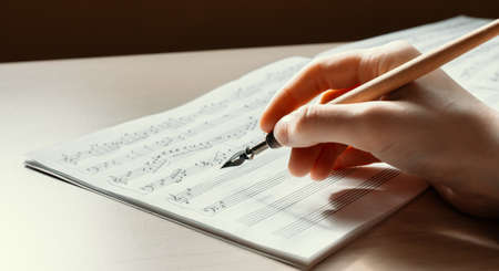 Woman's hand with a pen drawing notes in a music book, writing a melody by hand, composing musicの写真素材