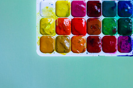 Palette with multicolored watercolor paints on a green background, creative background with paints