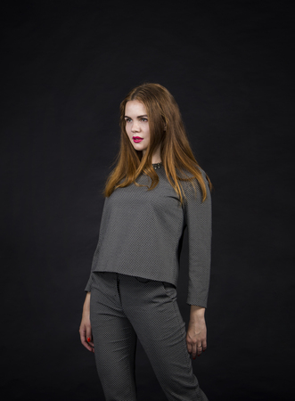 Red-haired girl with long hair in a pantsuit. Posing in the Studio on a dark background.の写真素材