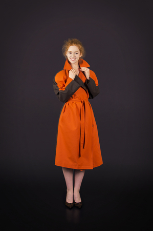 Beautiful, red-haired girl in an orange cloak posing. Studio shooting on a dark background.の写真素材
