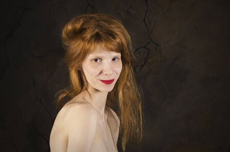 Portrait of a thin girl with bare shoulders, long,red hair and freckles on a dark background. The Studio is shot on a dark background.の写真素材