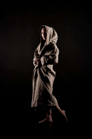 A young woman in a raincoat of coarse cloth on her naked body is isolated on a black background. Studio photography.の写真素材
