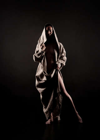 A young woman in a raincoat of coarse cloth on her naked body is isolated on a black background. Studio photography.の写真素材