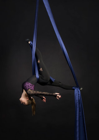A girl performs the acrobatic elements on silk. Studio shooting performances on a dark background.の写真素材