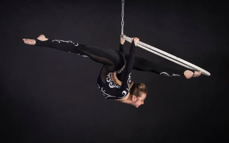 A young girl performs the acrobatic elements in the air ring. Studio shooting performances on a black background.の写真素材