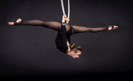 A young girl performs the acrobatic elements in the air ring. Studio shooting performances on a black background.の写真素材
