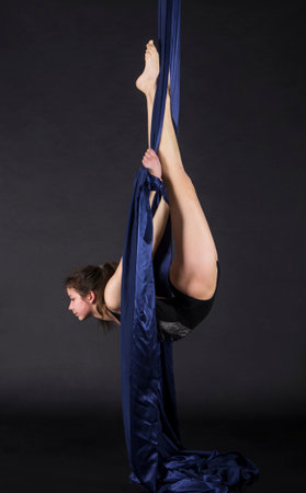 Young,smiling girl does exercises on the canvases. Studio recording of the performance on a dark background.の写真素材
