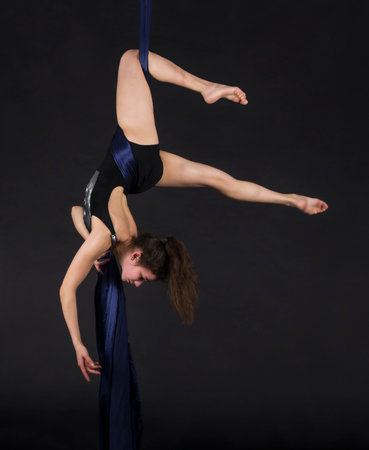 Young,smiling girl does exercises on the canvases. Studio recording of the performance on a dark background.の写真素材