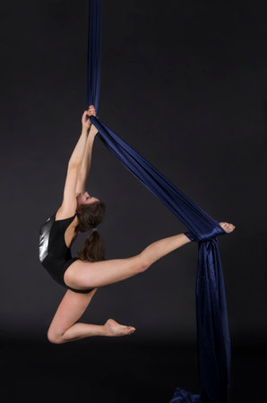 Young,smiling girl does exercises on the canvases. Studio recording of the performance on a dark background.の写真素材