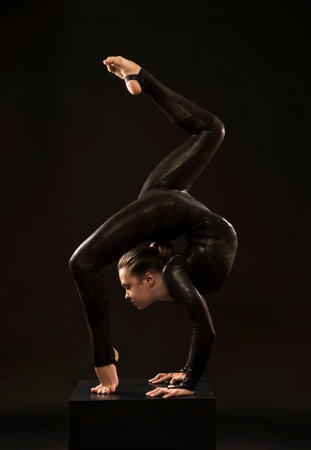 A charming girl gymnast, in a black suit, engaged in acrobatics in the light of the contra. Isolated...
