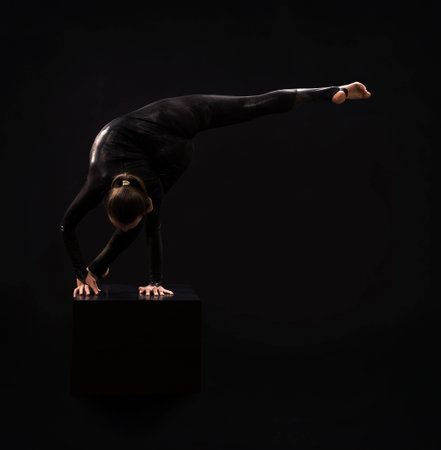 A charming girl gymnast, in a black suit, engaged in acrobatics in the light of the contra. Isolated images on a dark background.の写真素材