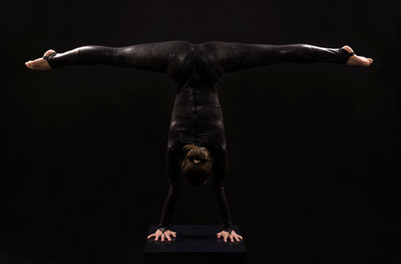 A charming girl gymnast, in a black suit, engaged in acrobatics in the light of the contra. Isolated images on a dark background.の写真素材