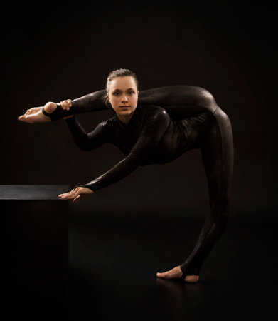 A charming girl gymnast, in a black suit, engaged in acrobatics in the light of the contra. Isolated images on a dark background.の写真素材