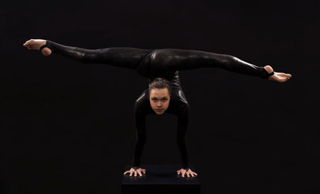 A charming girl gymnast, in a black suit, engaged in acrobatics in the light of the contra. Isolated...