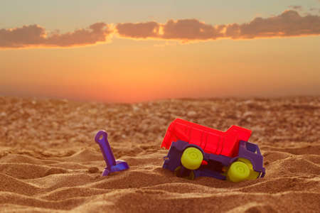 Concept. A toy car and a scoop are in the sand against the background of a beautiful sunset in the Dakar desert.の写真素材