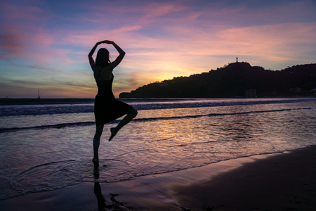 silhouette of woman practicing yoga on the beach at sunset.の写真素材